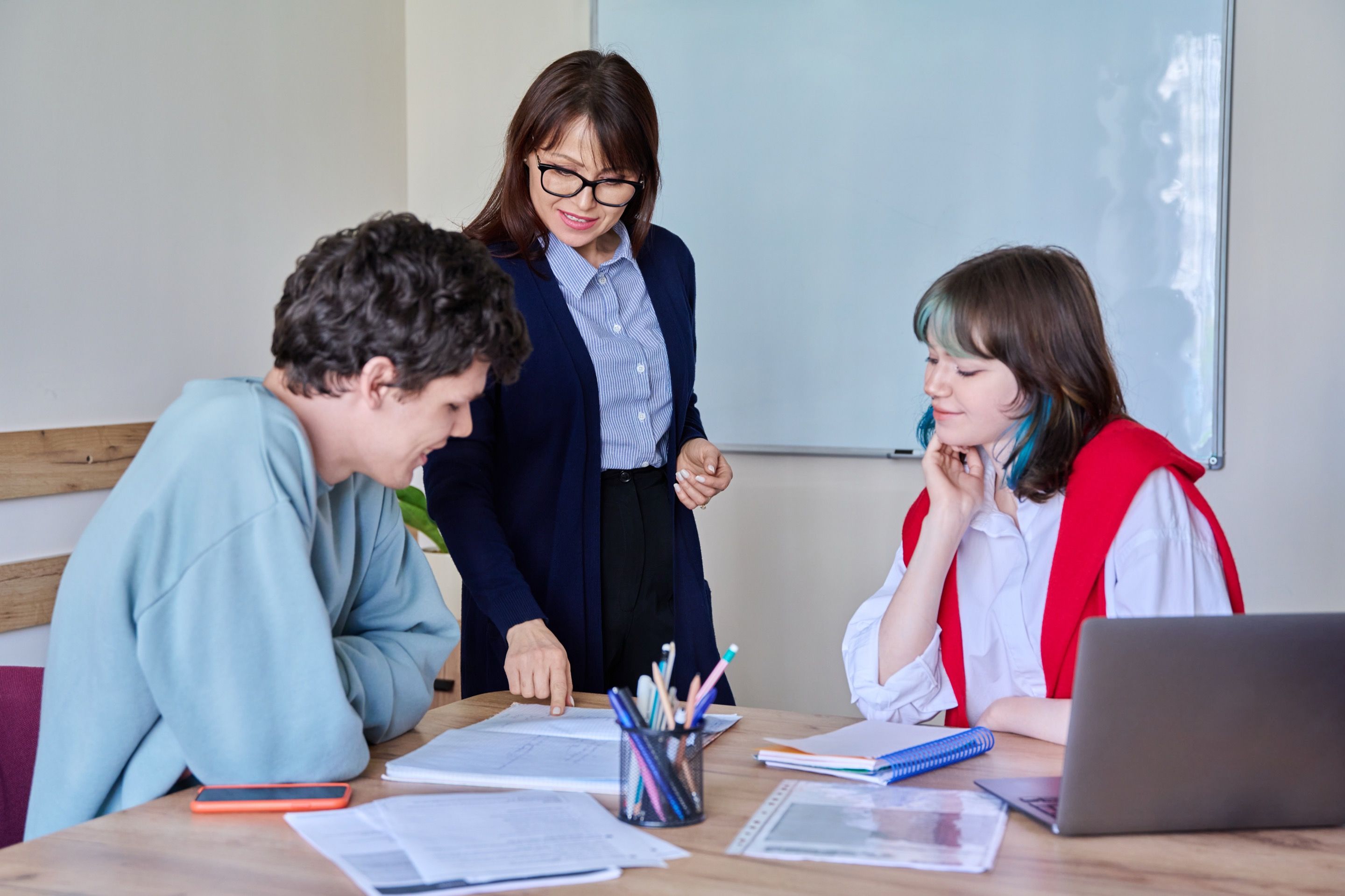Professora a orientar dois alunos durante uma sessão de estudo